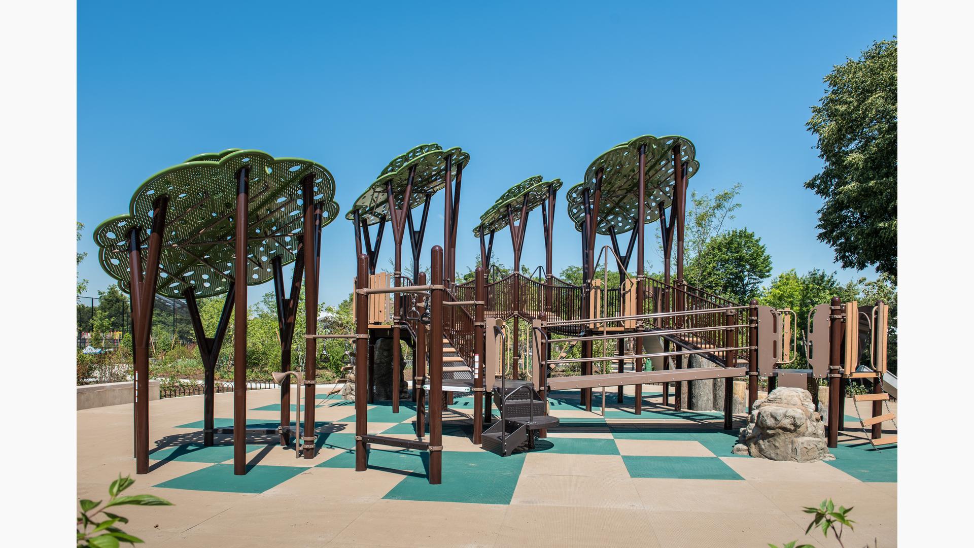 Custom tree structures tower over PlayBooster play structure. Log Steppers and rock climbers offer a realistic, natural look to the playground. Play area sits on a green and tan checkered ground surface.