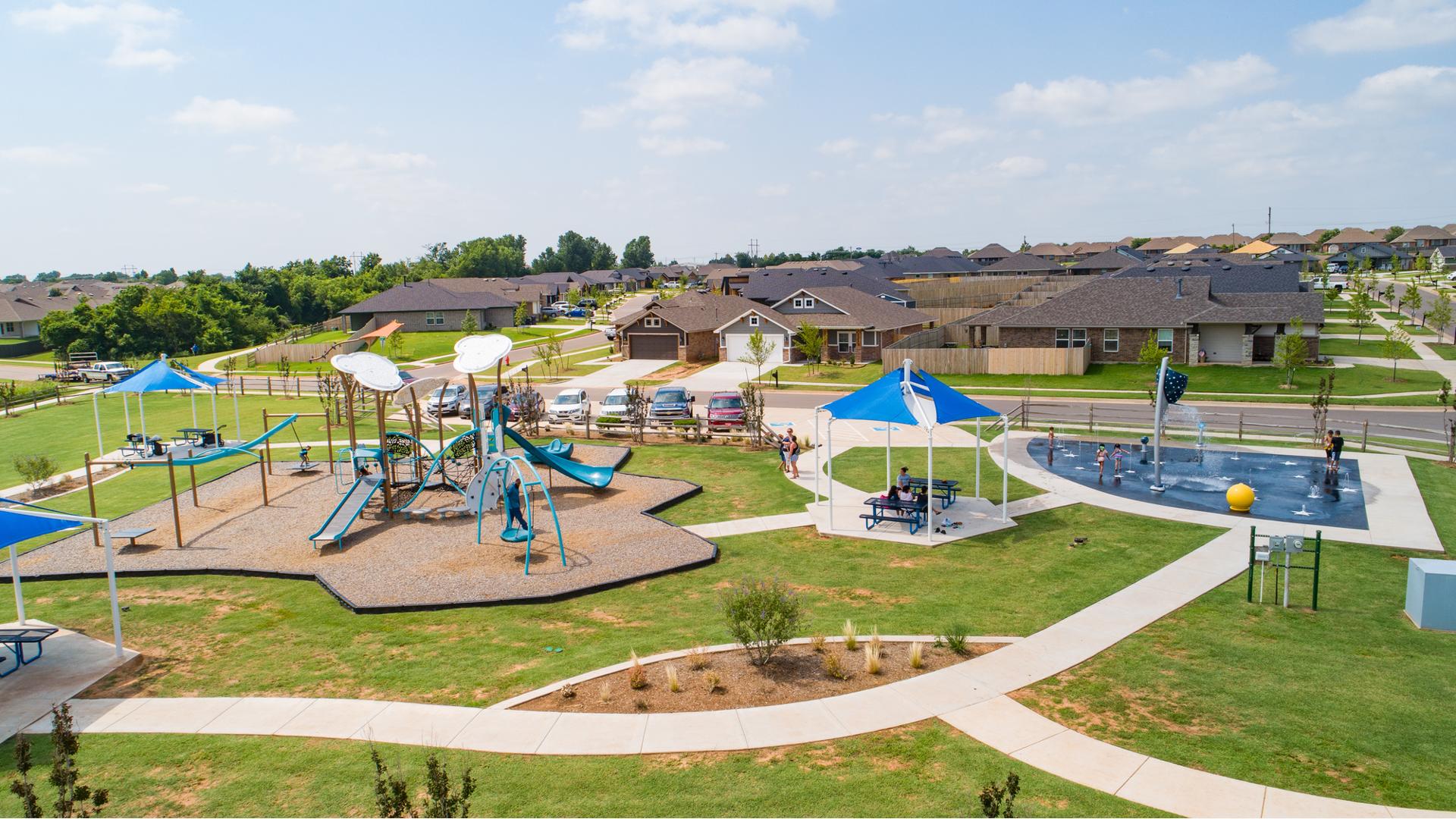 Elevated view of a community park with a cloud and wind themed playground on the left and a space themed splash pad on the right.