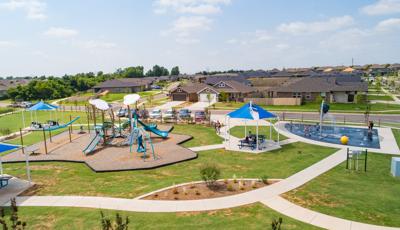 Elevated view of a community park with a cloud and wind themed playground on the left and a space themed splash pad on the right.