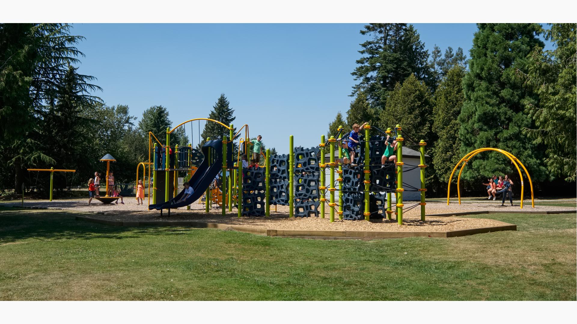 Children play at a brightly colored park playground with unique geometrically shaped climbers and other fun activities. 