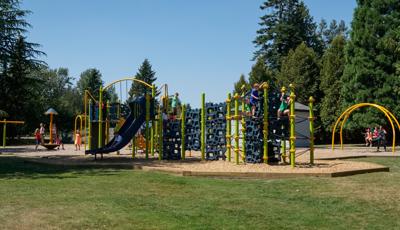 Children play at a brightly colored park playground with unique geometrically shaped climbers and other fun activities. 