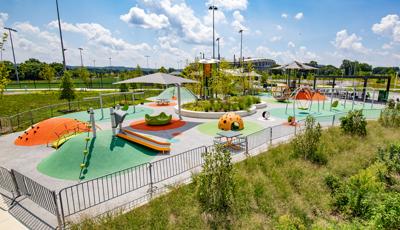 Large play space including merry-go-round, swings, sports-theme playground tower and a playground tower with shade. 