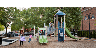 Two girls run toward play structure as a teenage girl looks down from a staircase. A boy attempts to go up the climbing wall to the top of the tower.