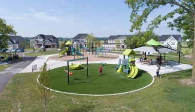 Kids of all ages playing on limon, gray and blue colored playgrounds in a neighborhood park and families gathered under picnic shelter. 