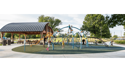 In Stagecoach Park two boys sit at the top of tehe Eclipse Net Climber. A dad helps his child on the Ribbon Slide and a little girl runs around the playground.