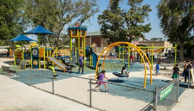 Bright green and orange playground with kids playing. Surfacing is a mix of blue rubber and sand. 