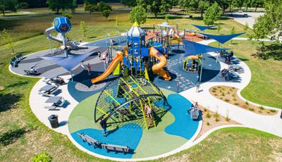 Full elevated view of a space themed playground filled with playing children. The playground safety surfacing is designed like planets, asteroid fields, moons, and stars. A playground tower designed like a rocket and a roof panel like a flying UFO.
