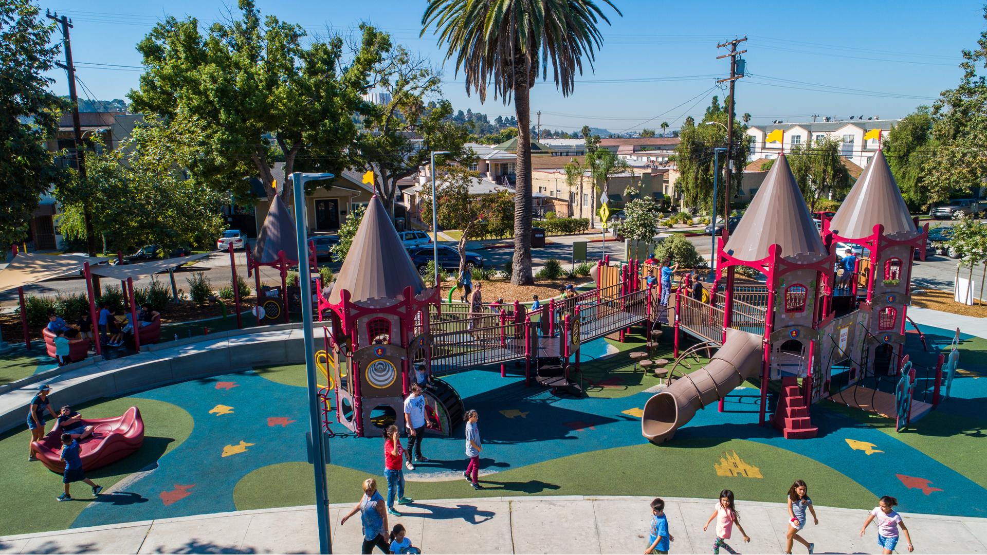 Children play all over an inclusive castle themed playground with safety surfacing designed like a mote flowing under and around the structure. 