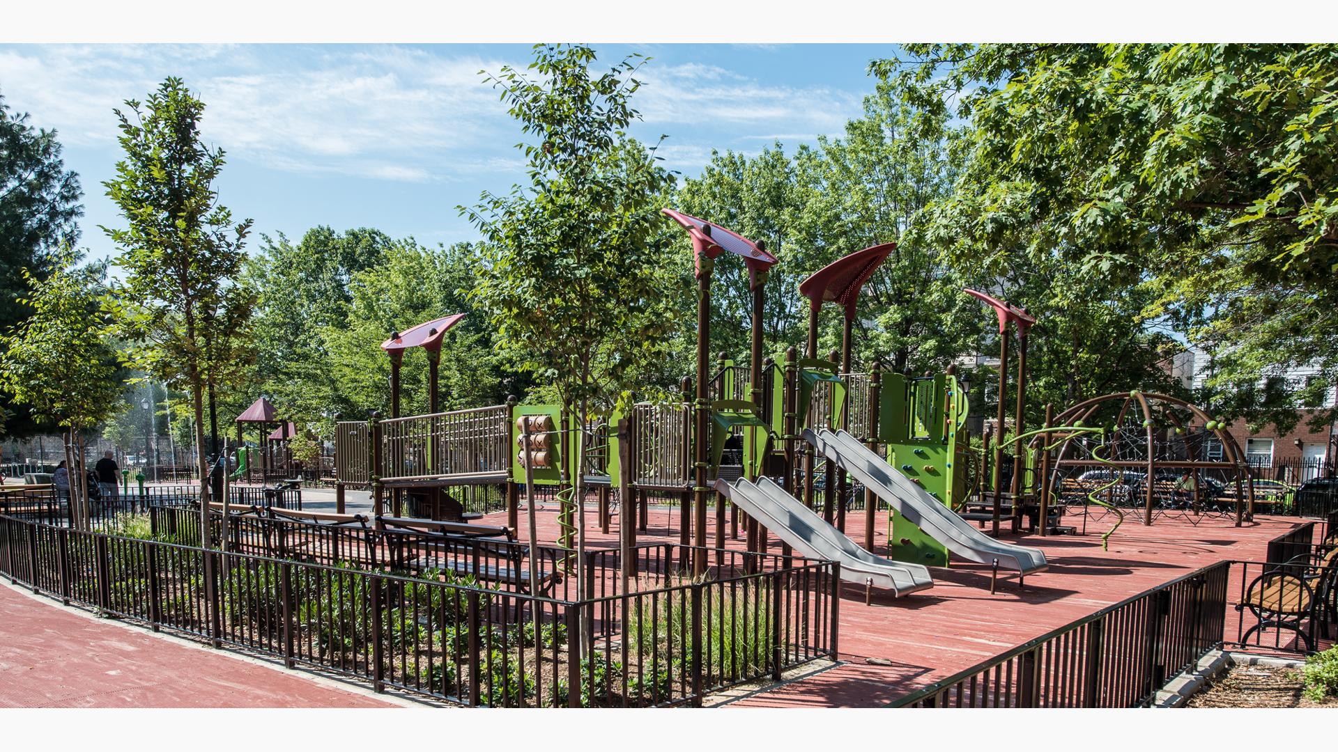 Playground camouflaged with the surrounding trees.  Playground includes triangle shaped roofs and stainless steel slides. 