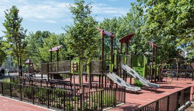 Playground camouflaged with the surrounding trees.  Playground includes triangle shaped roofs and stainless steel slides. 