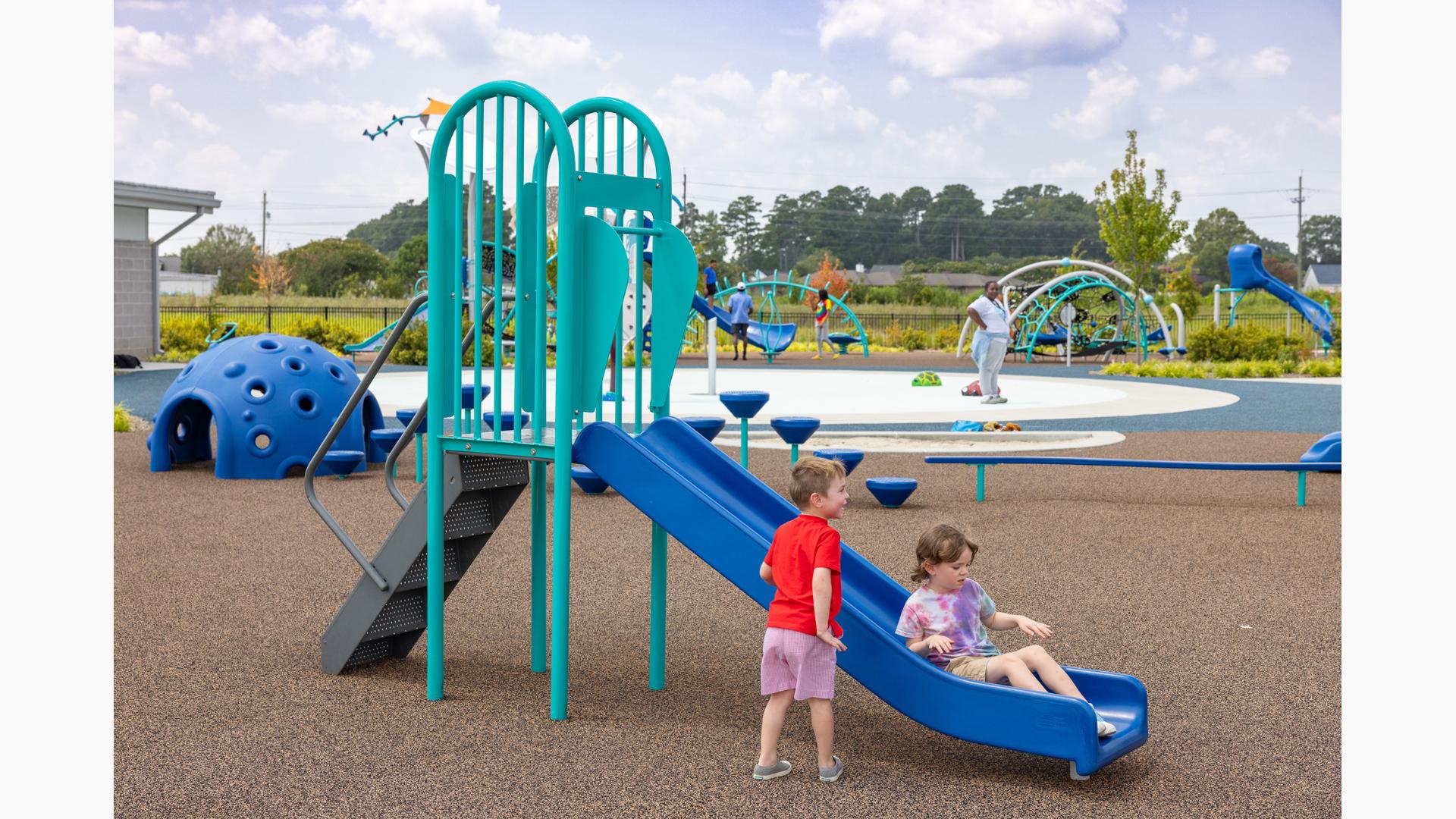 Young girl at the bottom of a freestanding playground slide with a boy nearby