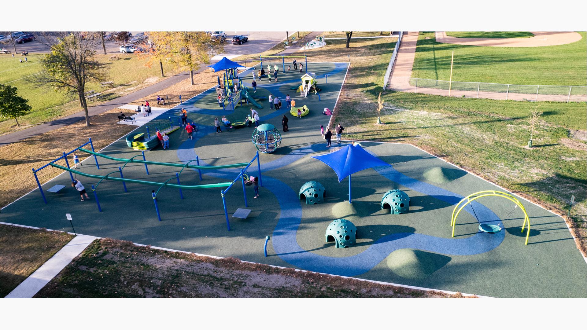 Large play area with inclusive safety surfacing has a main play structure with many other surrounding play activities like swing sets, zip lines and spinners.