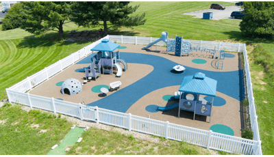 Elevated view of a square play space surrounded by a white picket fence with three separate play structures ranging accessibility from toddlers to twelve year old's.