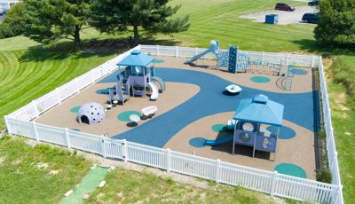 Elevated view of a square play space surrounded by a white picket fence with three separate play structures ranging accessibility from toddlers to twelve year old's.