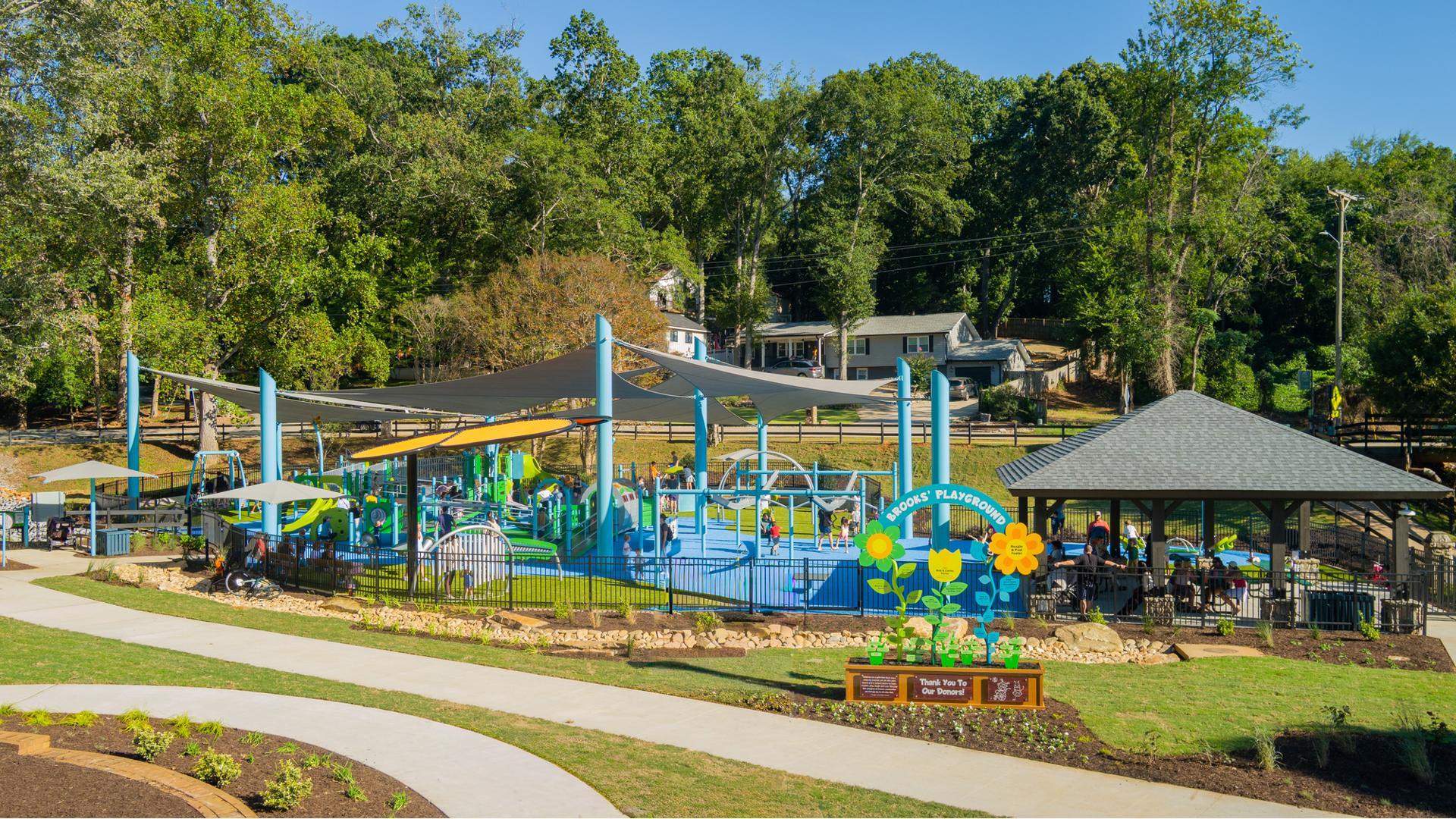 A large playground area with large grey shade sails overhead surrounded by black fencing.