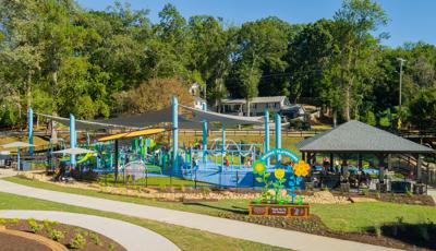A large playground area with large grey shade sails overhead surrounded by black fencing.