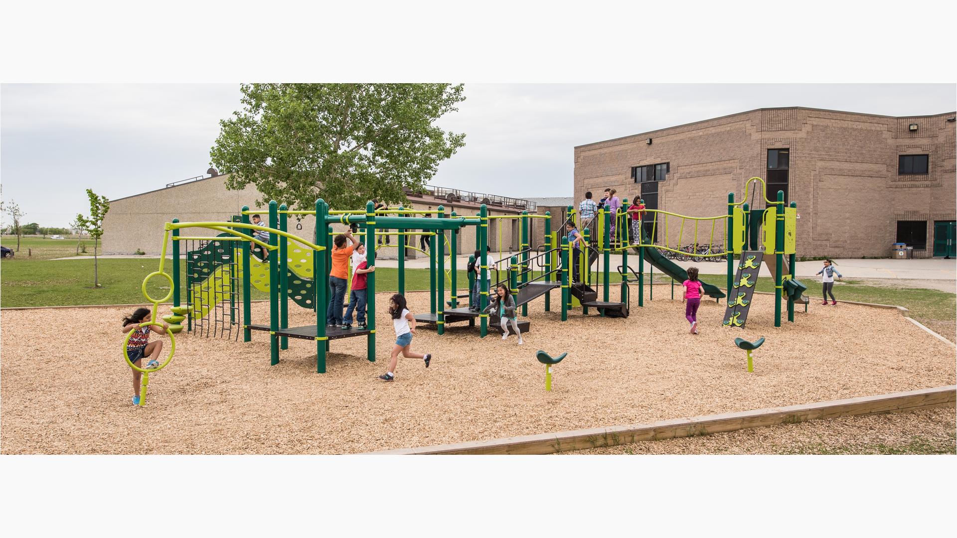 It is a cloudy day as kids at Stanley Knowles School play on the playground. A girl runs to the back of the line for the ZipKruz. Another girl uses the Gyro Twister Spinner. A group of children gather at the top of the slide.