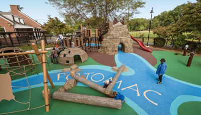 A woman stands on a replica of the Potomac river that lays on the grounds of Palisades Recreation Center park. It connects components of the playground as a family crossed the rope bridge.