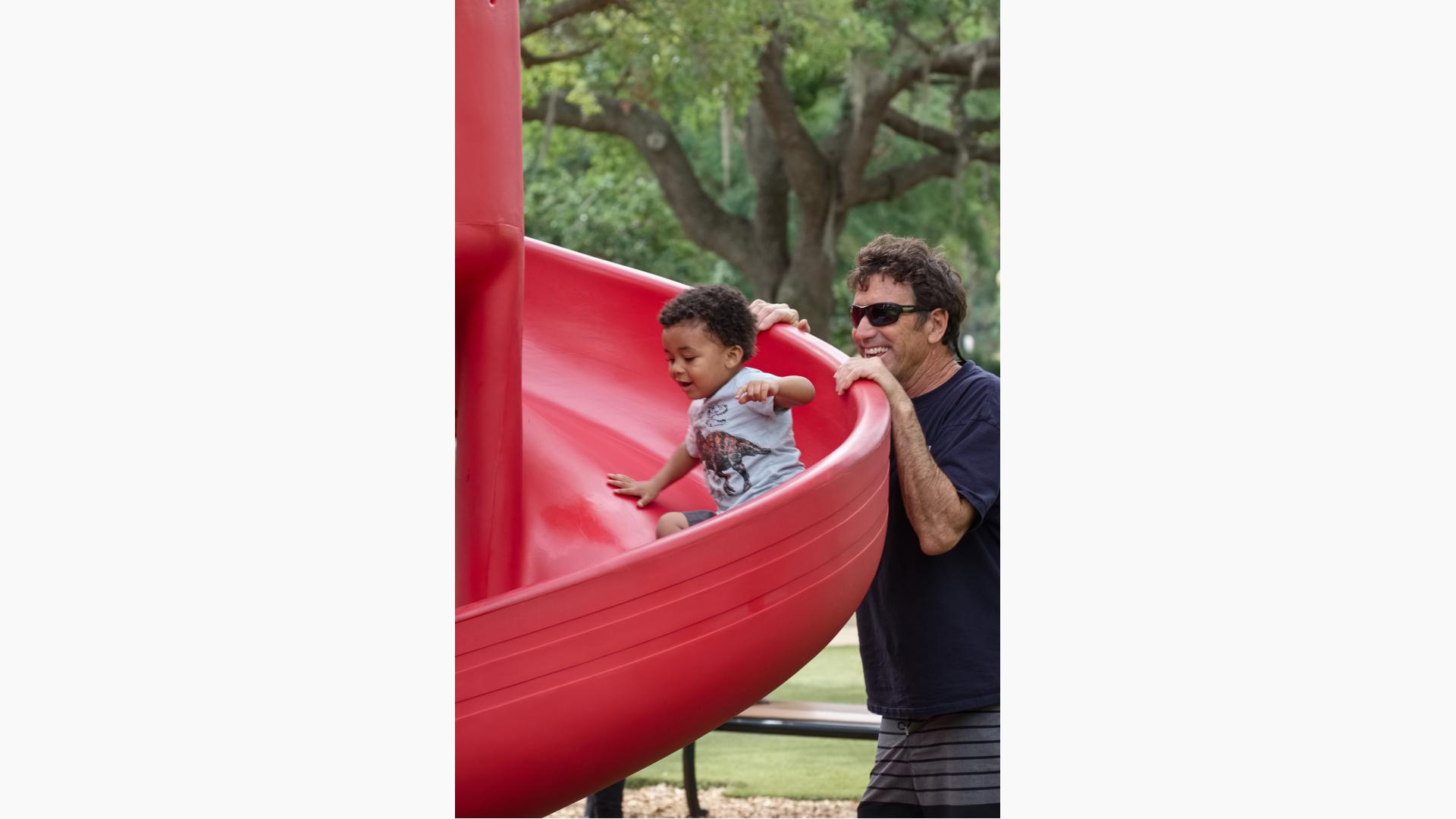 Dad watches boy ride down slide