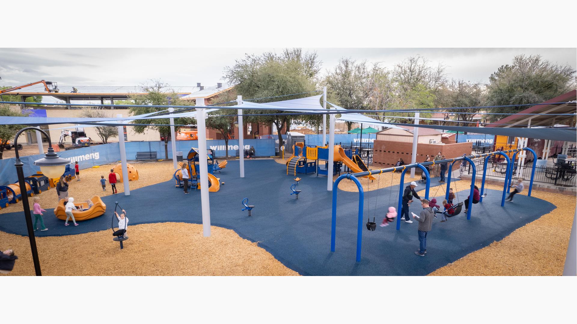 Elevated view of children playing on a playground with large blue shade sails overhead.