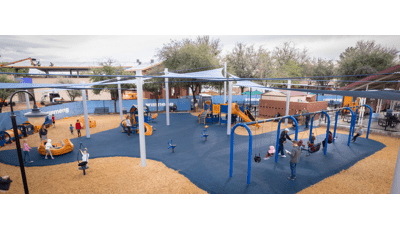 Elevated view of children playing on a playground with large blue shade sails overhead.