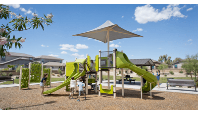 Parents watch their kids have fun on new playground. Two boys climb a logo climber, while an older girl encourages a toddler girl to ride down the double slide.