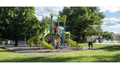 Dad watches his son ride down Double slide as other kids climb rock climber feature. A boy in blue jumps off of Gemini slide.