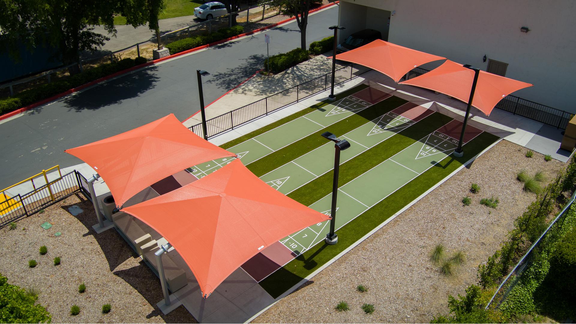 Elevated view of three outdoor shuffle board lanes with two burnt orange square shades covering the ends of the lanes.