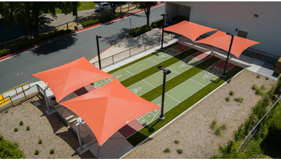 Elevated view of three outdoor shuffle board lanes with two burnt orange square shades covering the ends of the lanes.