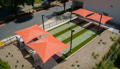 Elevated view of three outdoor shuffle board lanes with two burnt orange square shades covering the ends of the lanes.