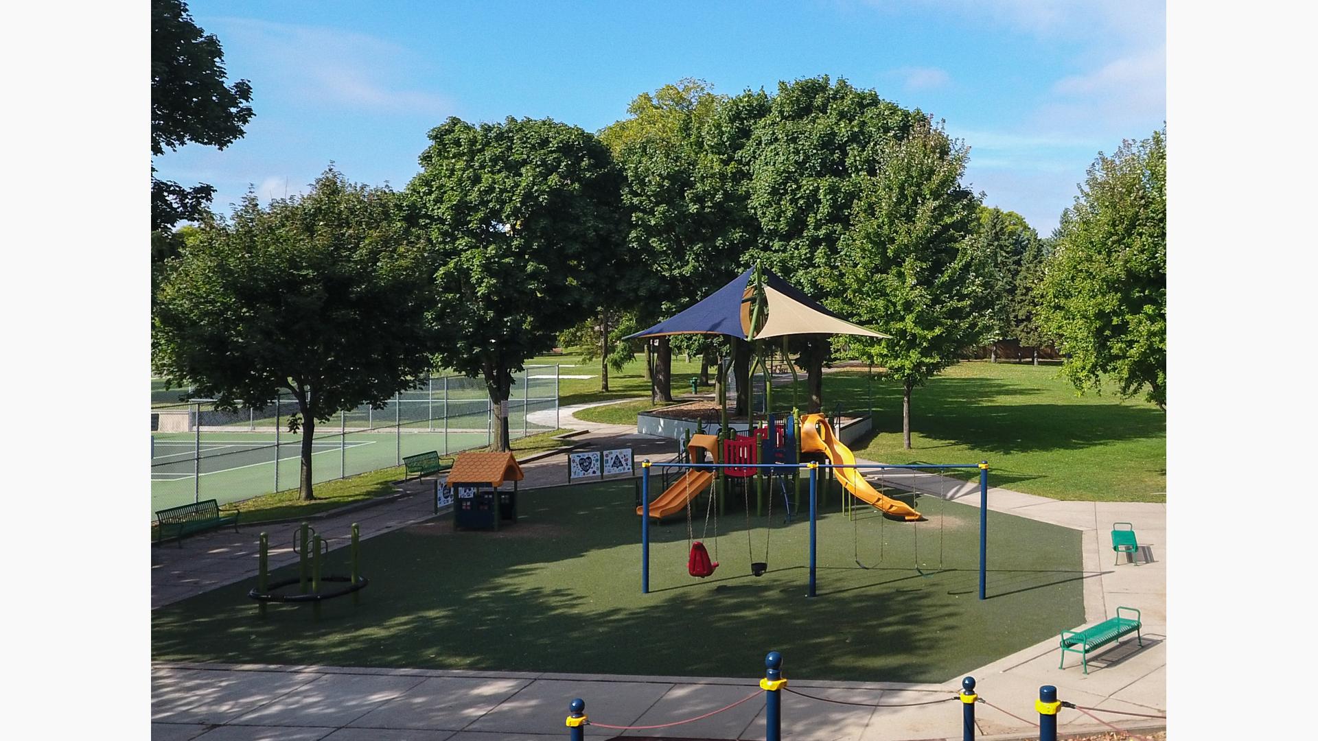 Primary colored playground with shade above playground structure. Includes swings and other freestanding play elements with artificial grass surfacing. 