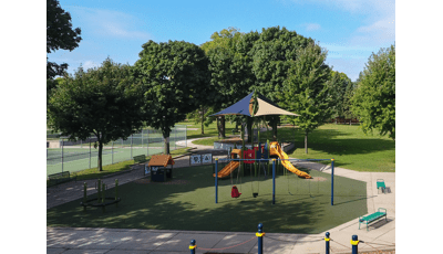 Primary colored playground with shade above playground structure. Includes swings and other freestanding play elements with artificial grass surfacing. 