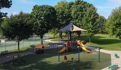 Primary colored playground with shade above playground structure. Includes swings and other freestanding play elements with artificial grass surfacing. 