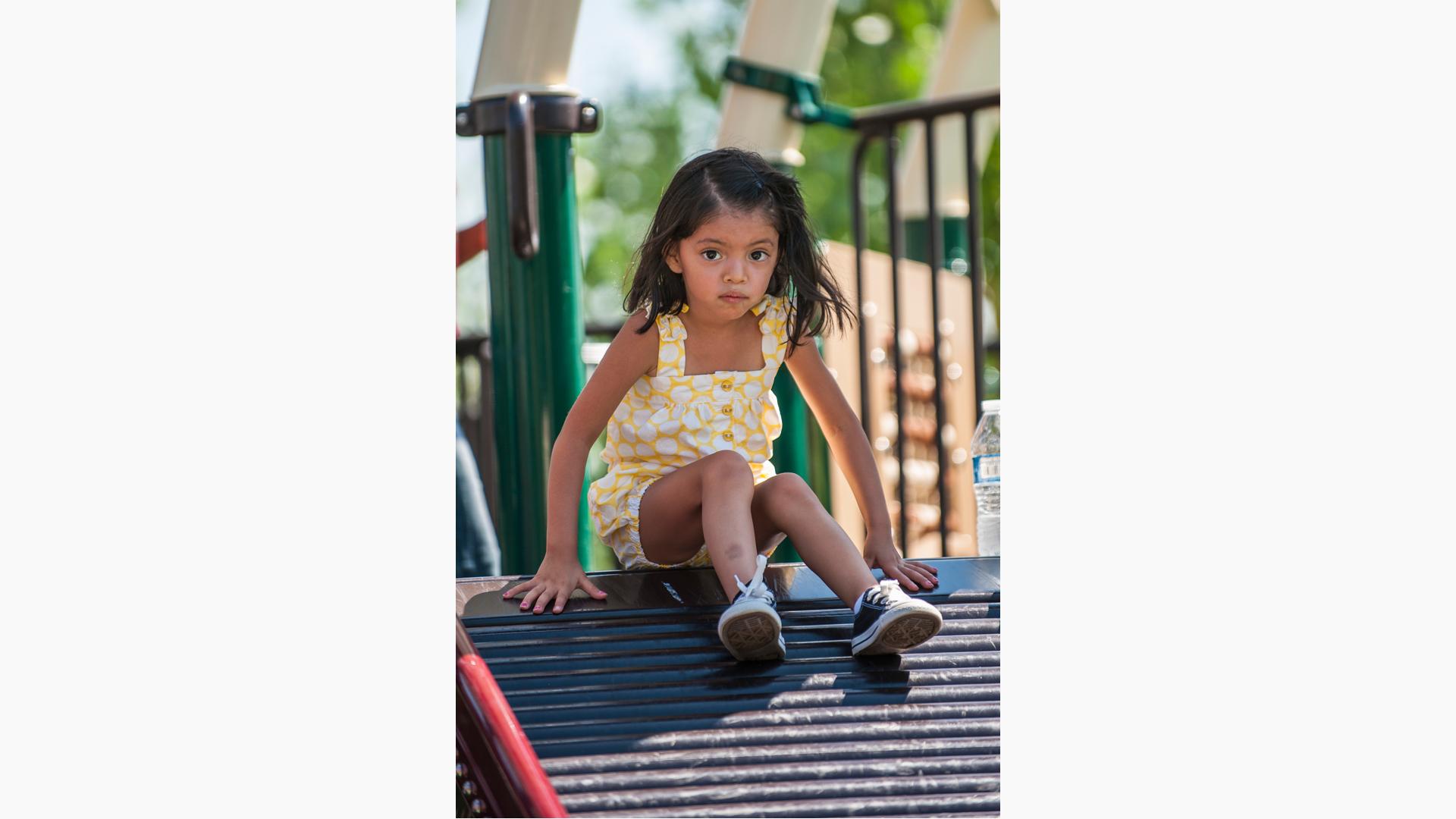 Girl in yellow outfit sitting on top of rollerslide