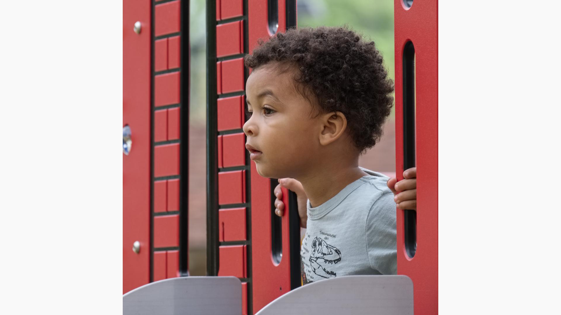 Toddler boy sticks his head out of play structure