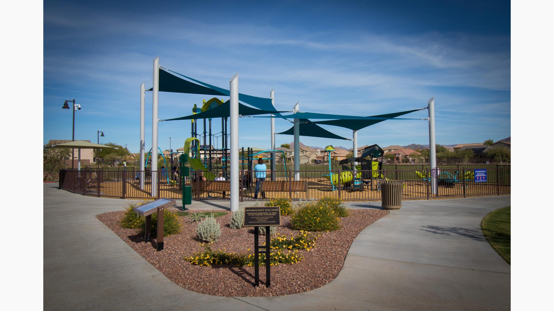 Parents watch from benches as their kids play on the PlayBooster and Smart Play  play systems. SkyWays shade panels cover the playground.