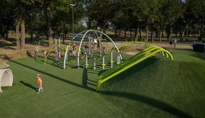 Children climb and play on the ropes of a unique play structure with additional connected spinners, bridges, climbers, and artificial grass underfoot.