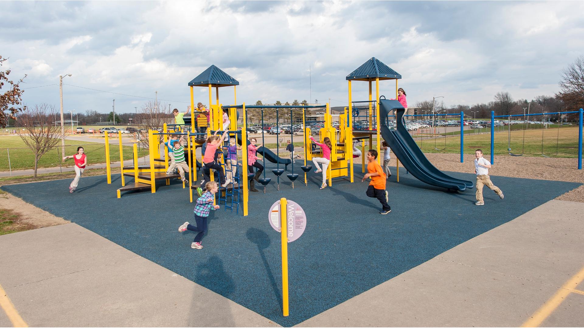 despite the wind and clouds, children at Notre Dame Elementary run and and play on  PlaySense  play structure. 