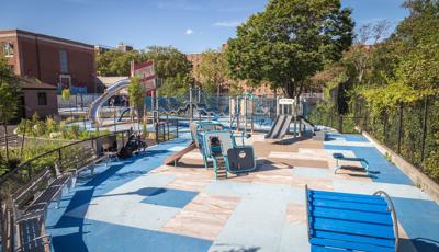 Red-striped playground tower with stainless steel slide and connects to a wavy looking bridge.  Play space also includes a geometric square smaller structure for younger kids.