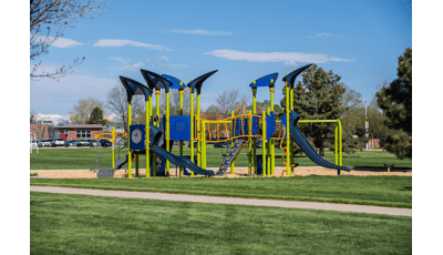 A playground with lime green posts and blue accents on the other playground activities set next to a school and it's parking lot. 