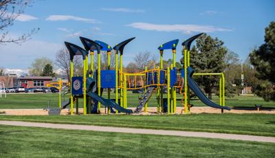 A playground with lime green posts and blue accents on the other playground activities set next to a school and it's parking lot. 