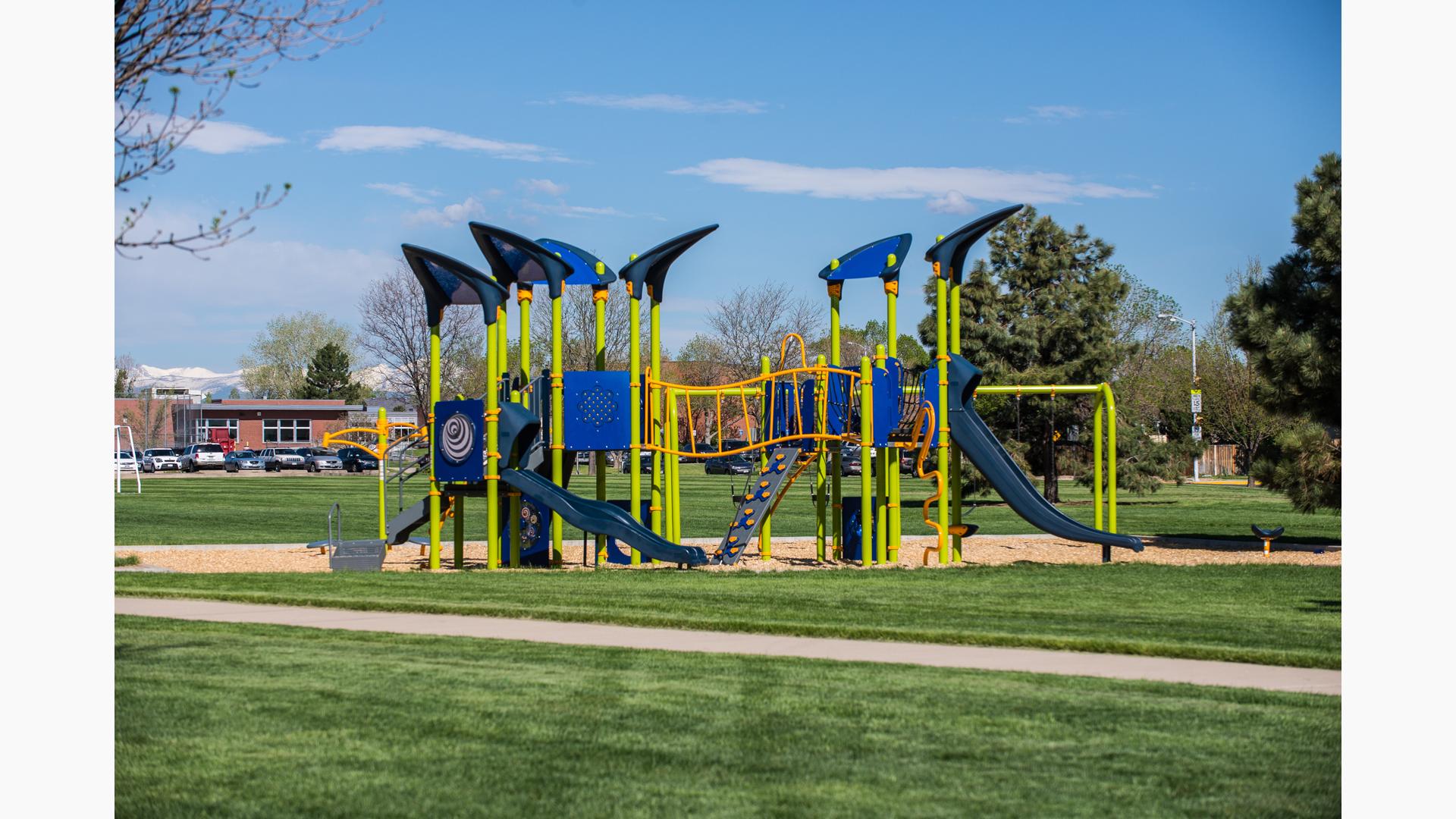 A playground with lime green posts and blue accents on the other playground activities set next to a school and it's parking lot. 