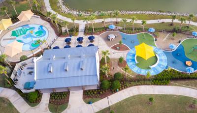 Bird's eye view of a playground play area connected to a splash pad next to a lakeside.