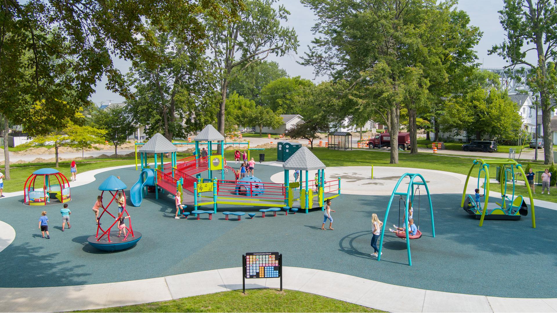 Side view of a inclusive play area with a main structure equipped with accessible ramps all surrounded by other accessible spinners and swings.