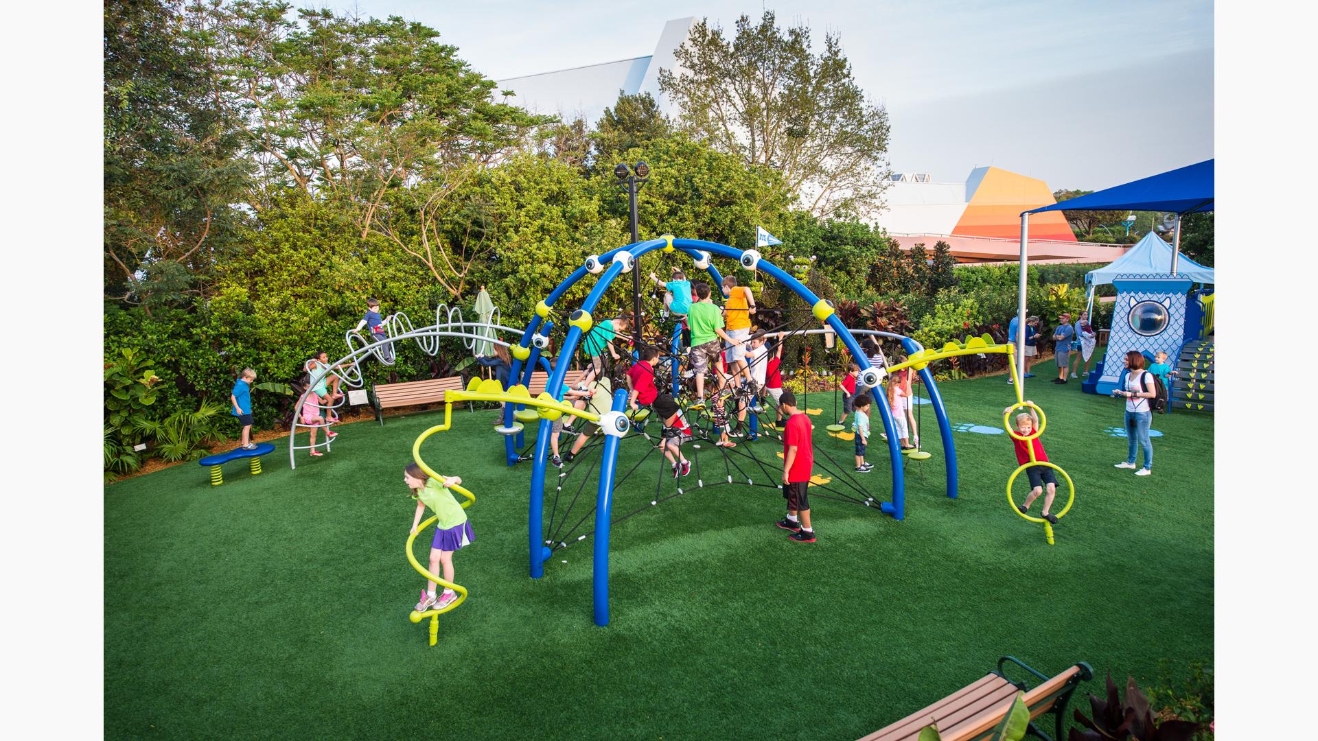 Children climber and play on crisscrossed ropes connected to blue arched posts with custom connectors designed as eyeballs playing into the playground's movie theme of Mosters Inc.