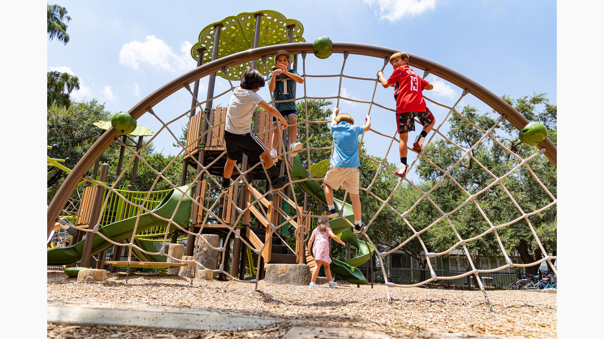 Children climbing on arched cargo net with with a nature theme playground in the background.