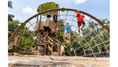 Children climbing on arched cargo net with with a nature theme playground in the background.