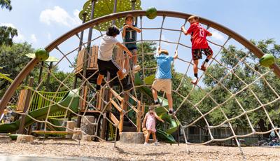 Children climbing on arched cargo net with with a nature theme playground in the background.