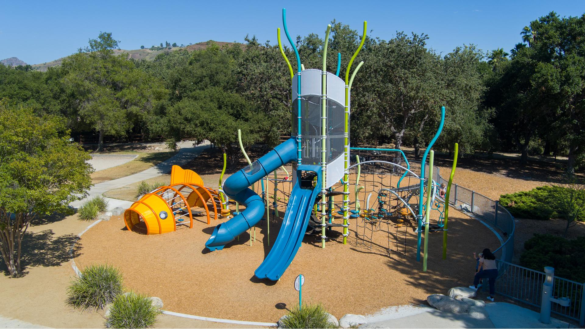 Elevated view of a large tower structure filled with multiple different attached play activities next to a custom play structure designed like a orange fish.