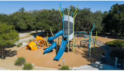 Elevated view of a large tower structure filled with multiple different attached play activities next to a custom play structure designed like a orange fish.